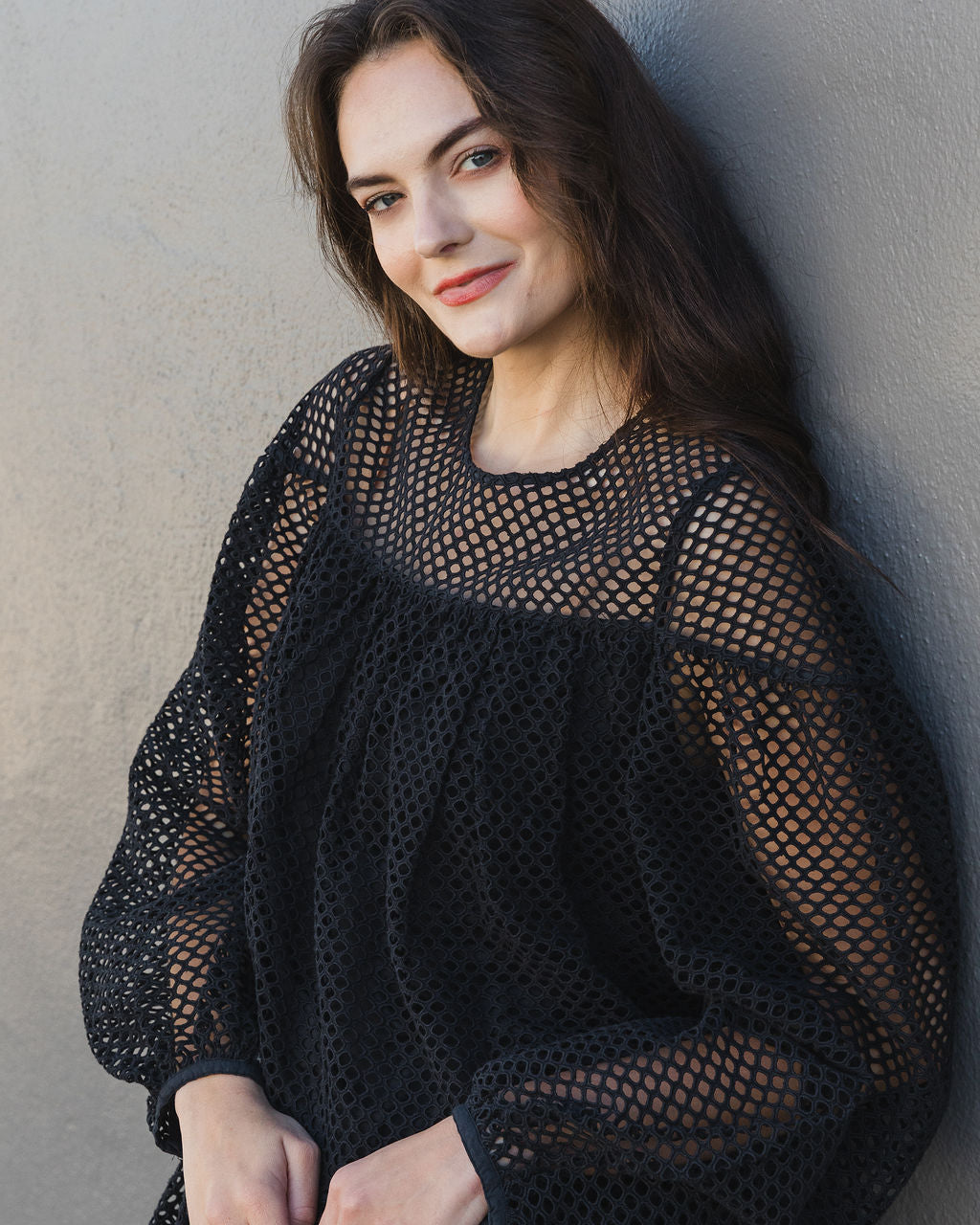 Woman wearing a black mesh top against a plain background