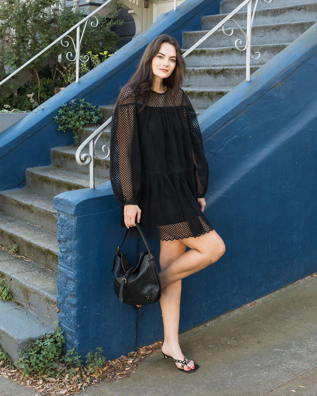Woman in a black dress standing on steps with a blue wall and white railing.