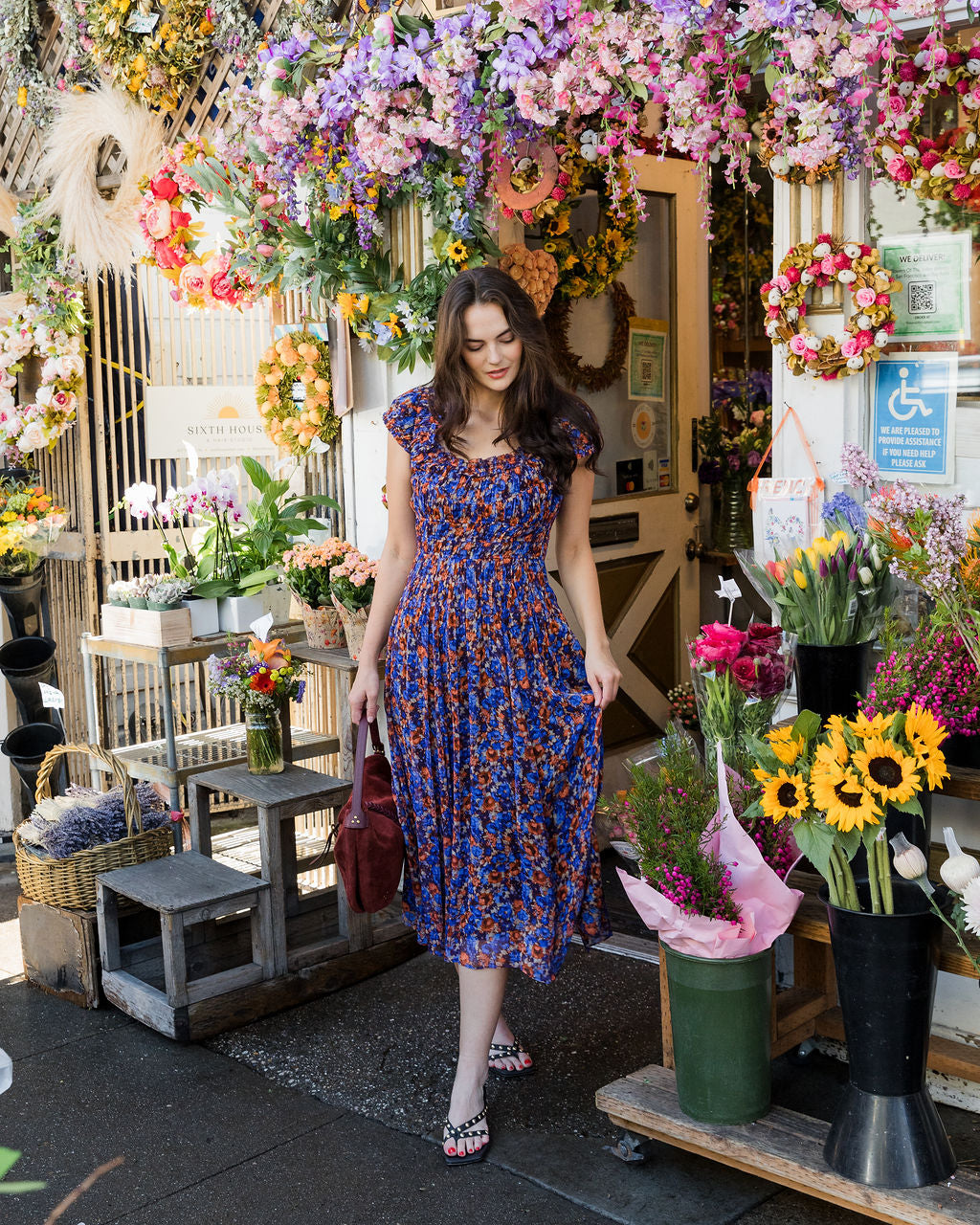 Woman in a floral dress standing in a flower shop with various flowers and plants.