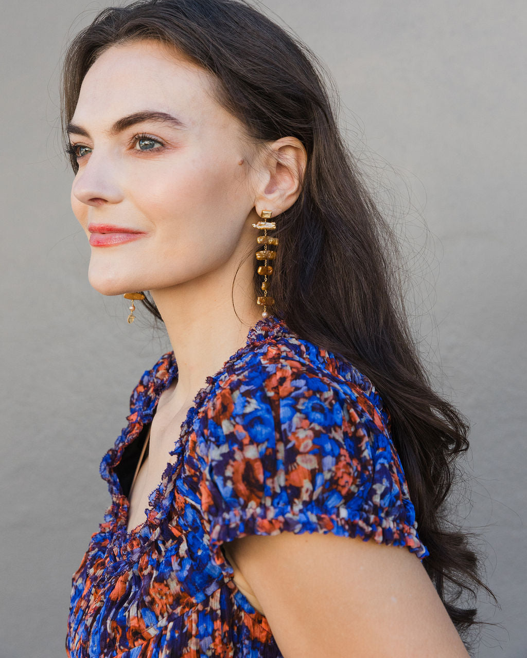 Woman wearing a blue and orange patterned top with gold earrings against a gray background
