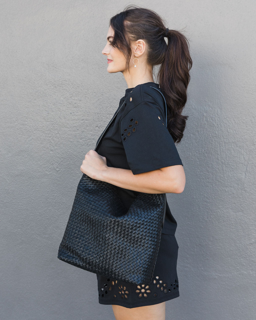 Woman holding a black textured bag against a gray wall