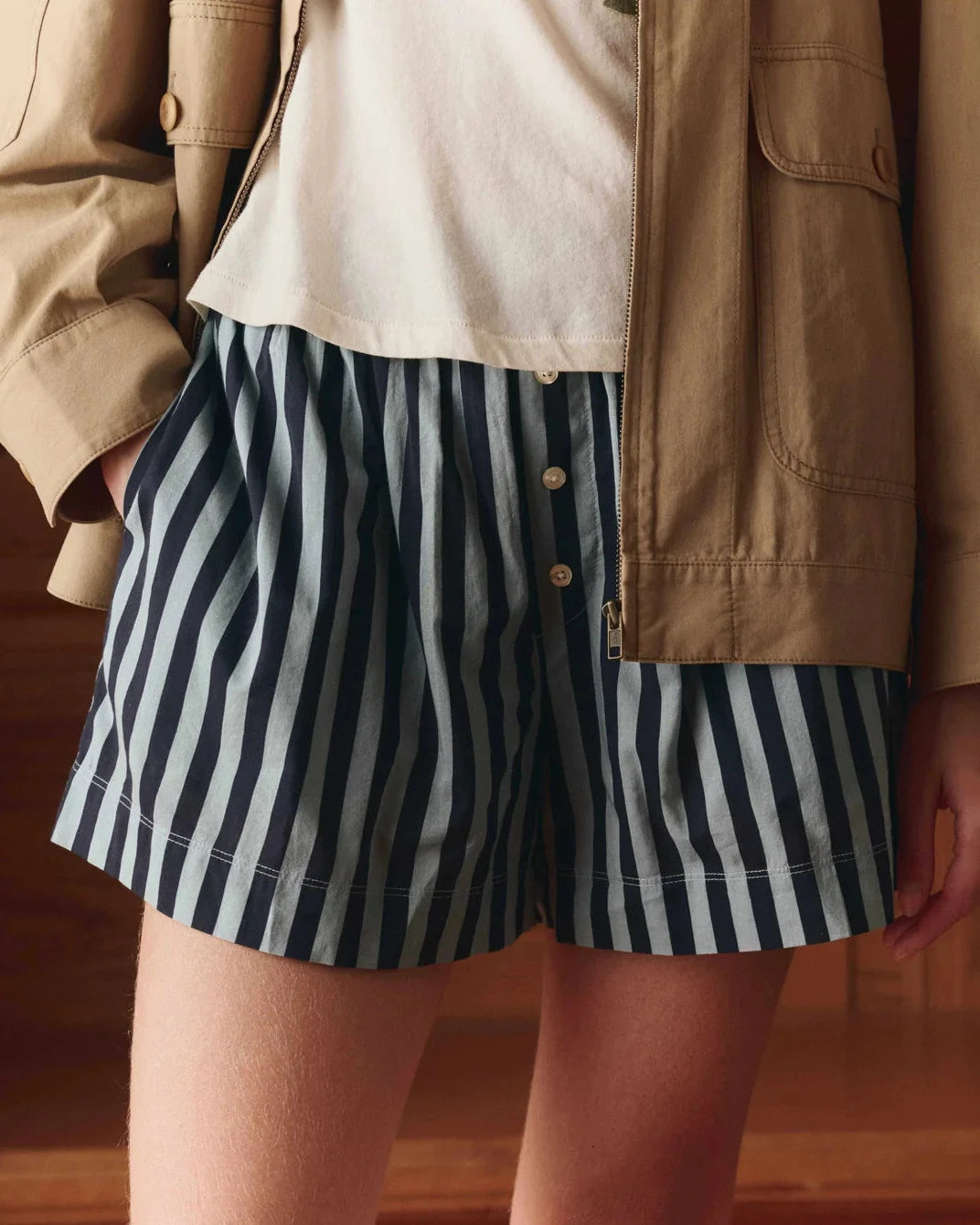Person wearing navy and white striped shorts with a beige jacket.