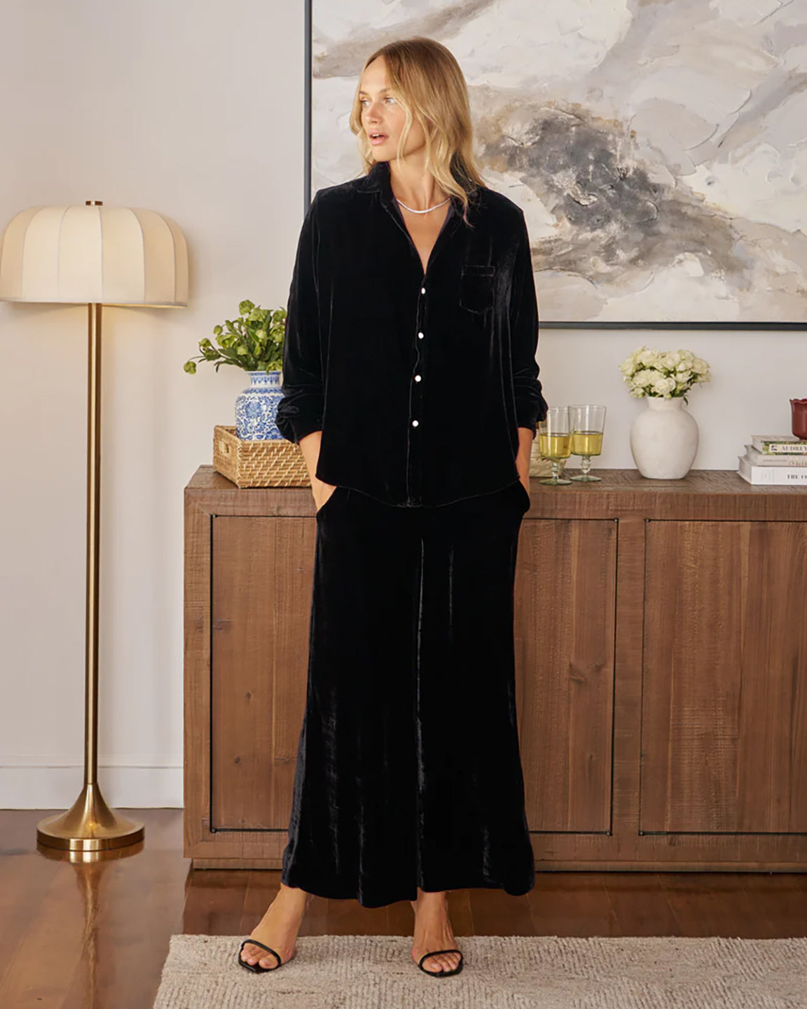 Woman in black velvet outfit standing in a stylish room with decor elements.