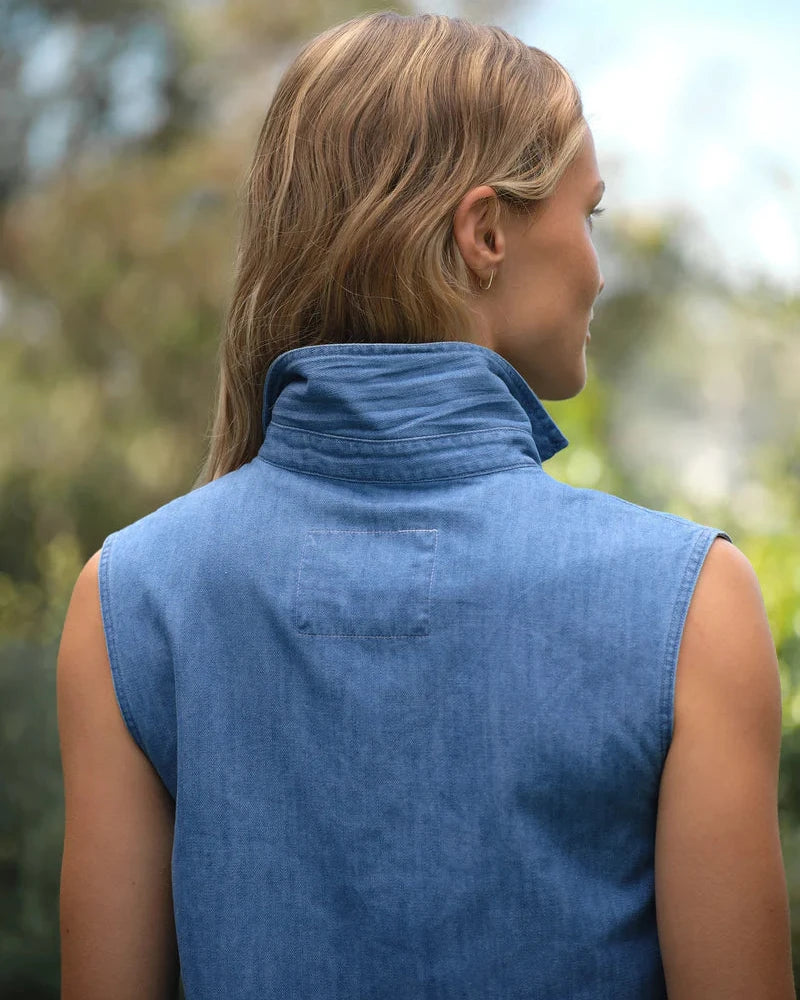Person wearing a blue sleeveless jacket with a blurred natural background