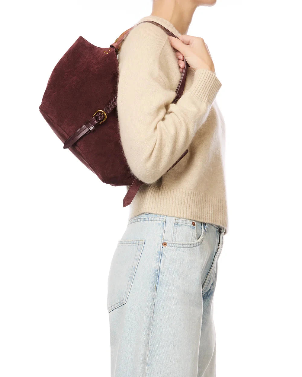 Person wearing a beige sweater and light blue jeans, holding a burgundy backpack.