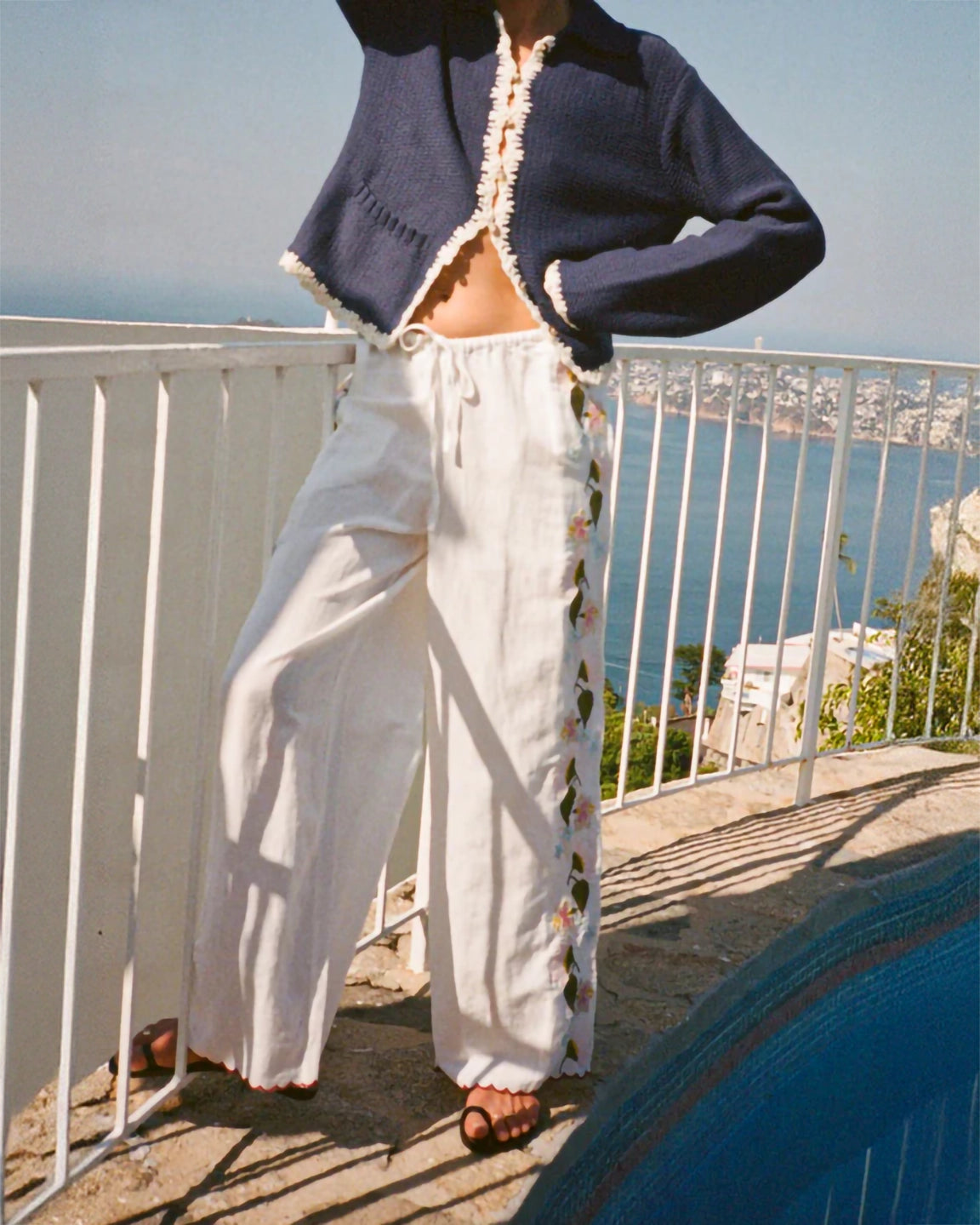 Person wearing a navy cardigan and white pants with a scenic background