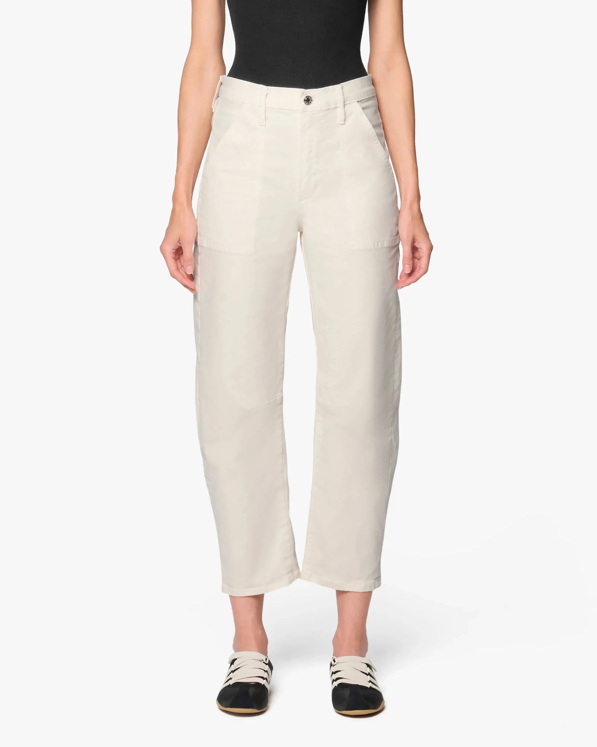 A model wearing a pair of off-white cropped trousers with a black bodysuit and black-and-white slide sandals, shown against a plain light gray studio background.