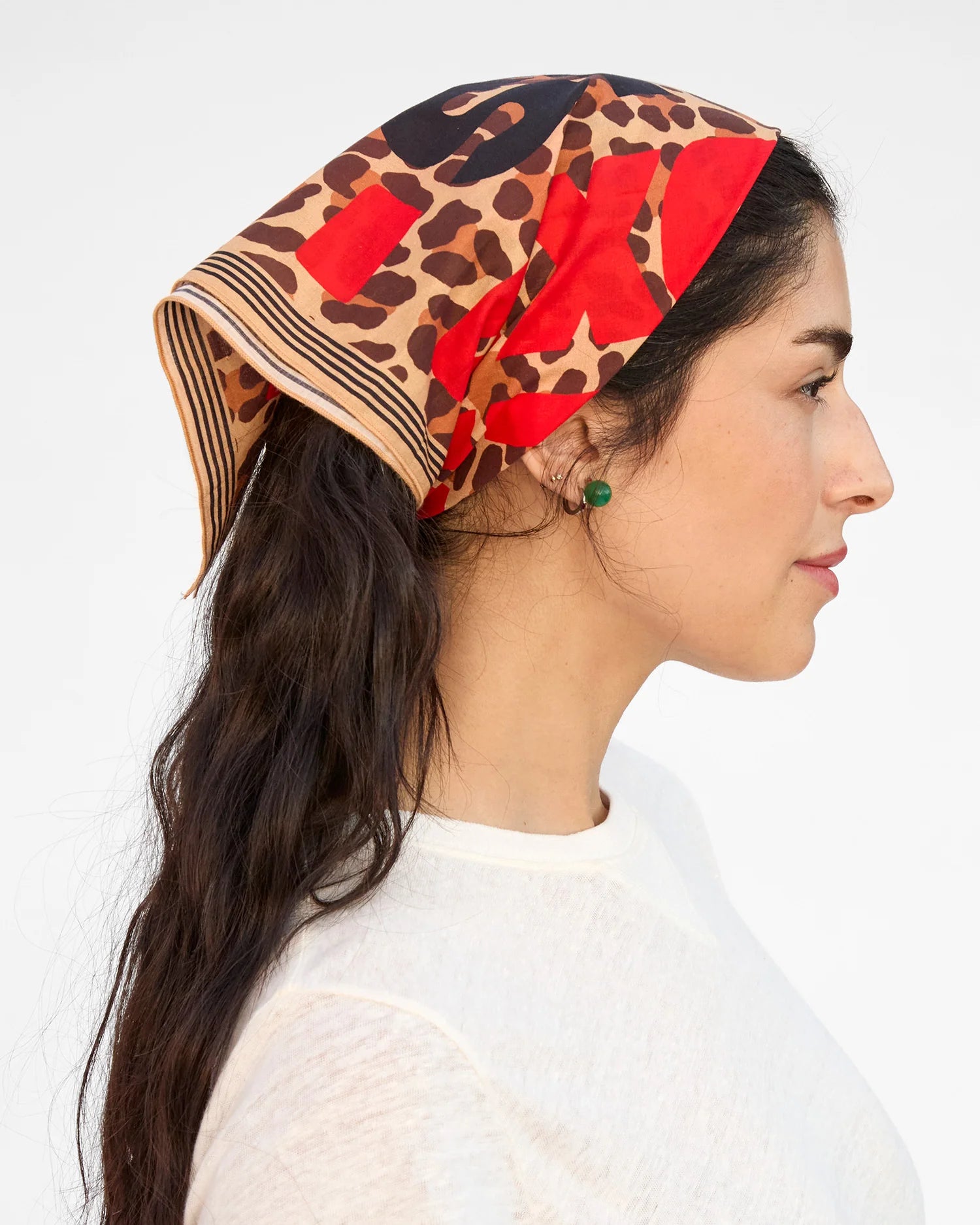 Woman wearing a colorful headscarf with a pattern of red, black, and brown on a white background