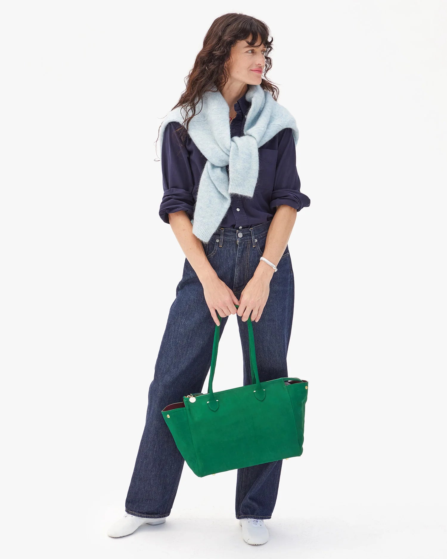 Woman holding a green bag wearing a blue outfit with a light blue scarf on a white background