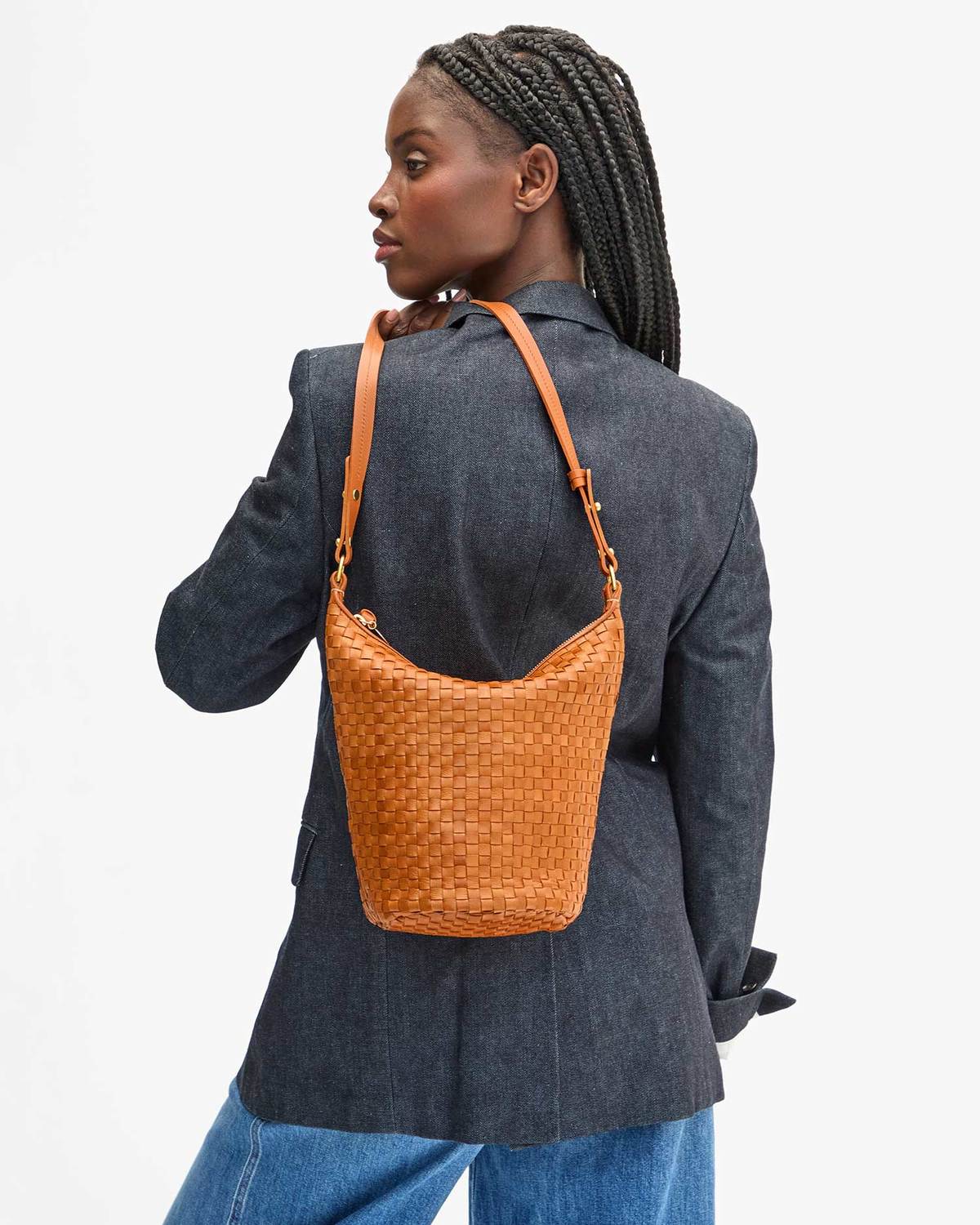 Person wearing a woven brown bag over one shoulder on a white background
