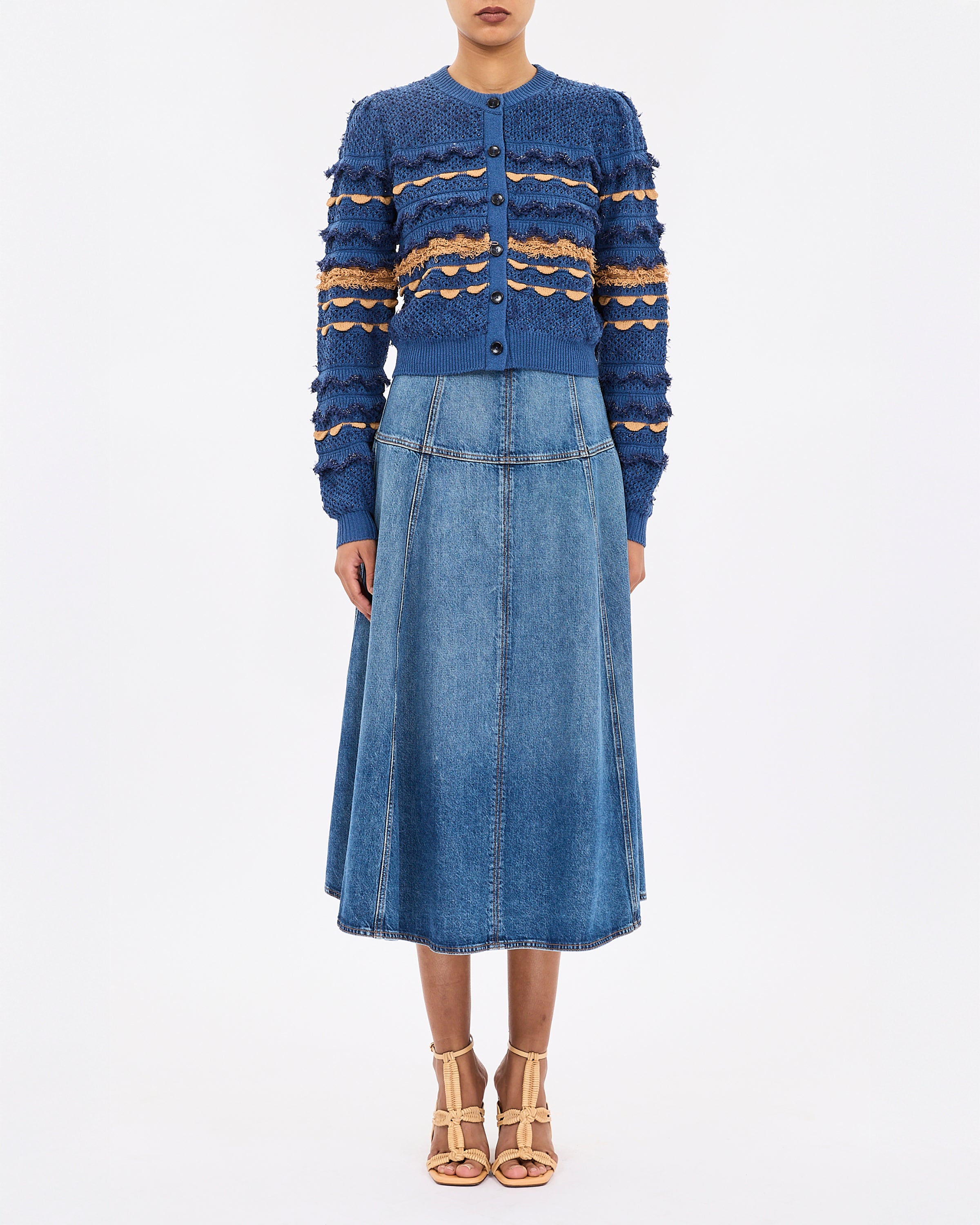 Person wearing a blue patterned cardigan and denim skirt on a white background