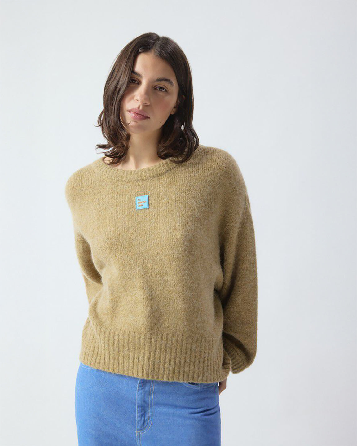 Woman wearing a beige sweater with a small blue logo on a white background