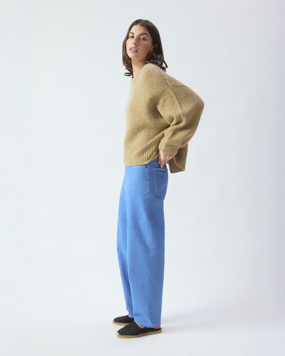 Person wearing a beige sweater and blue pants on a white background