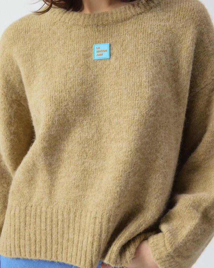 Person wearing a mustard yellow sweater with a blue label on a white background