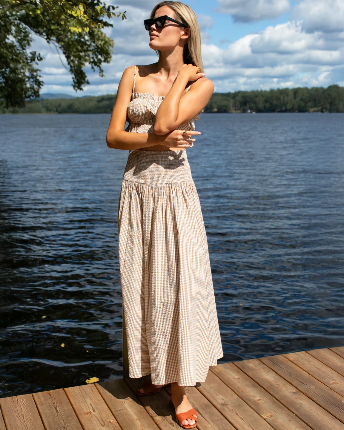 Woman in a beige dress standing on a wooden dock by a lake
