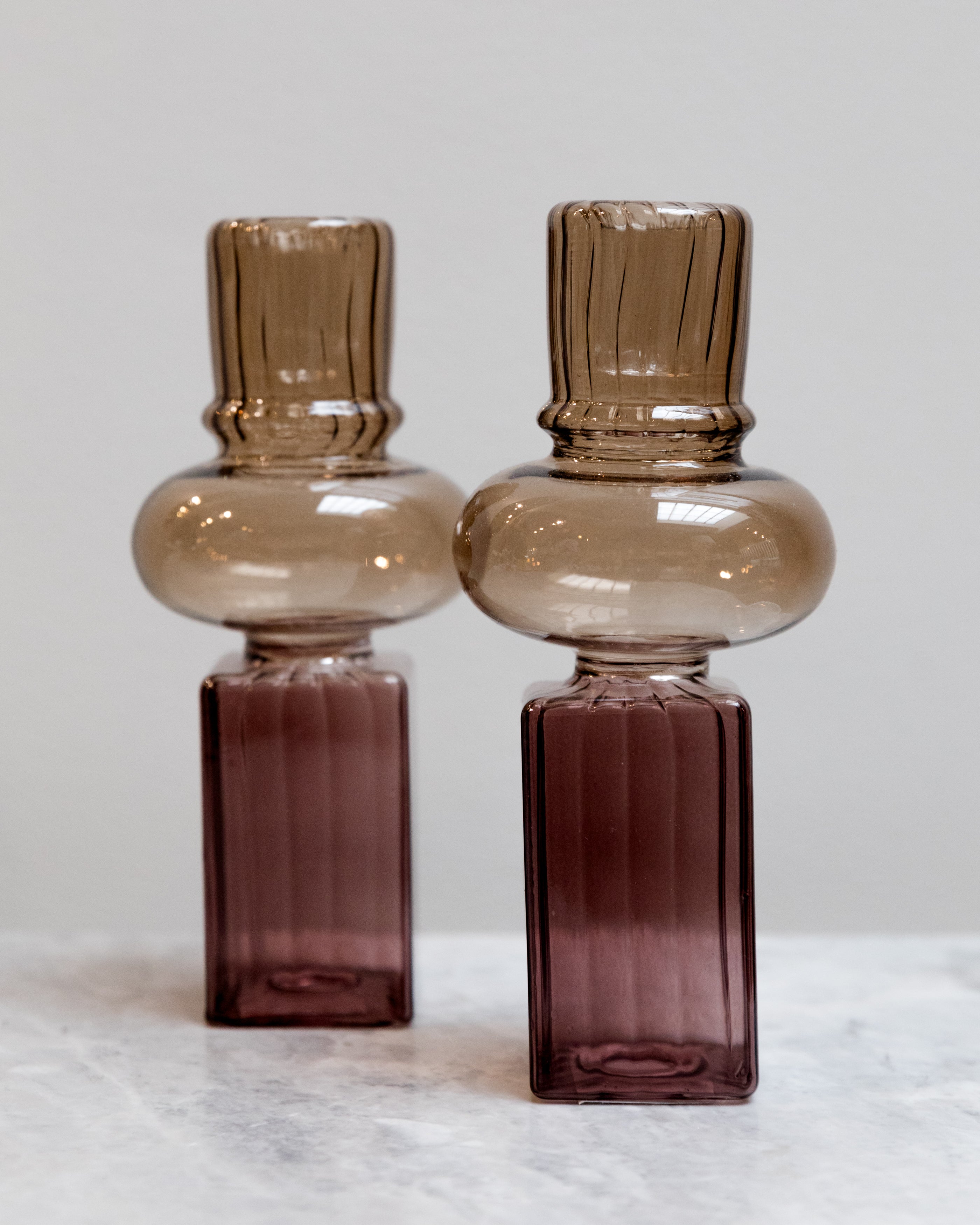 Two glass bottles with brown and purple gradient on a light gray background