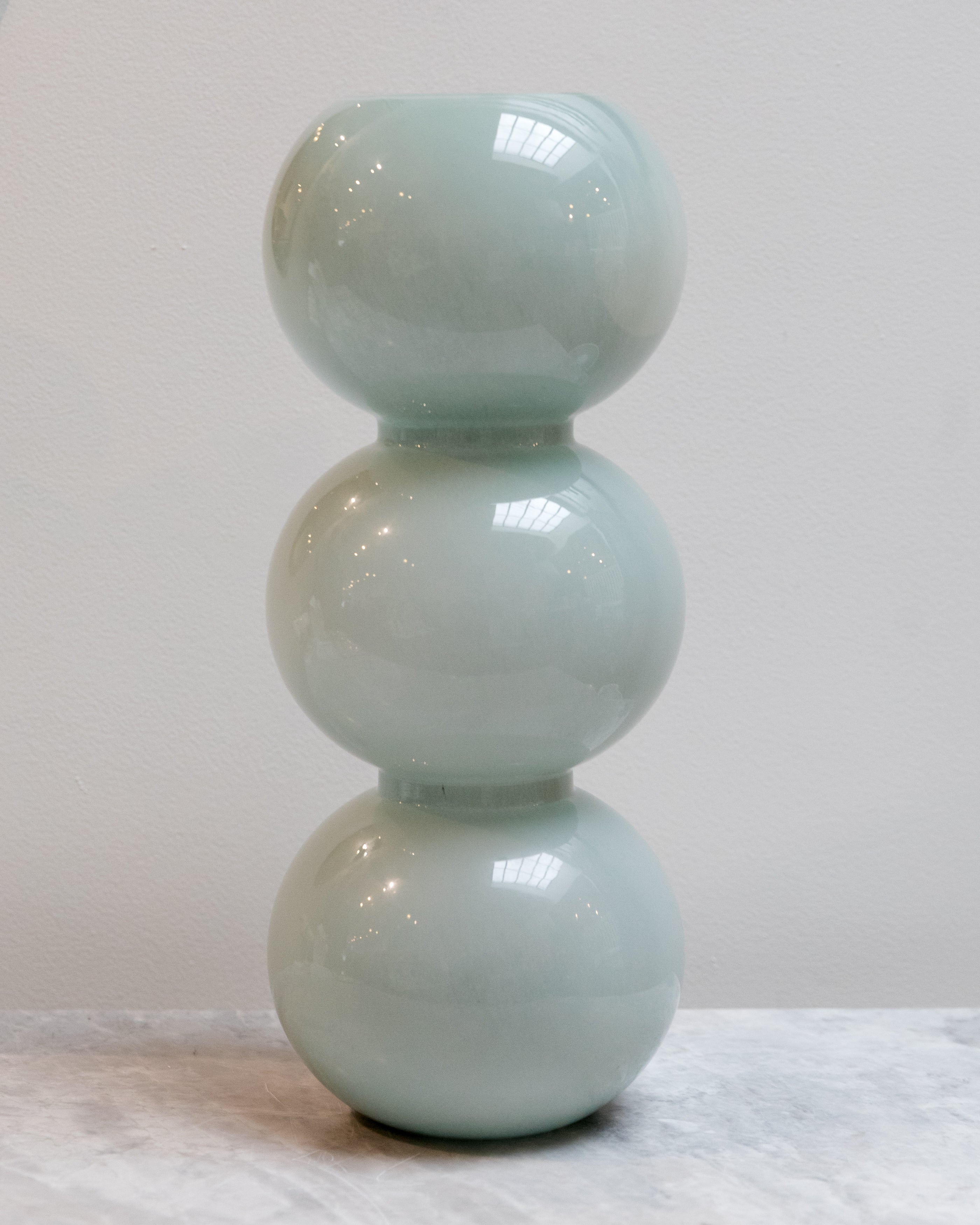 Light blue ceramic vase with three stacked spheres on a white surface.