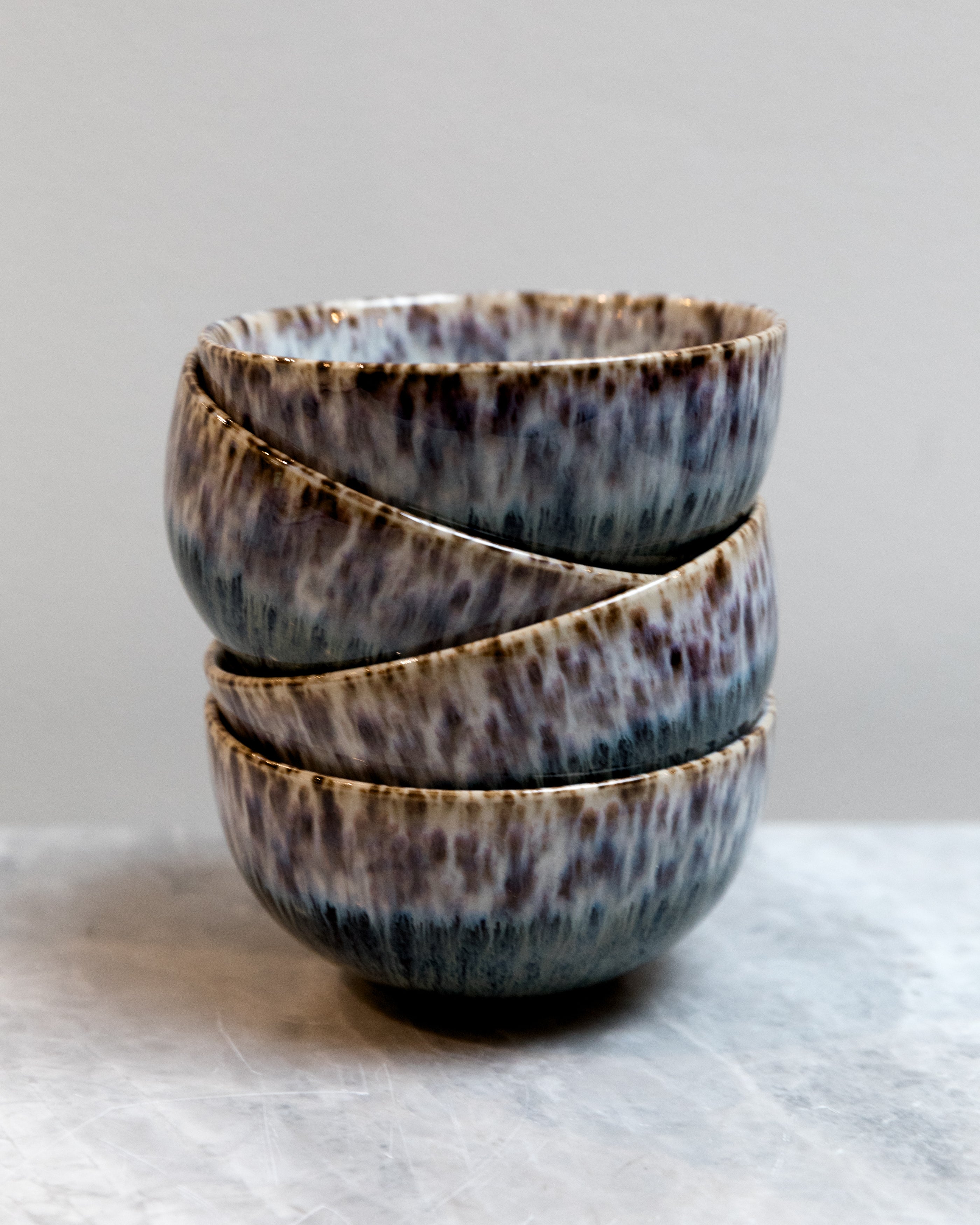 Stack of three ceramic bowls with speckled glaze on a light gray background