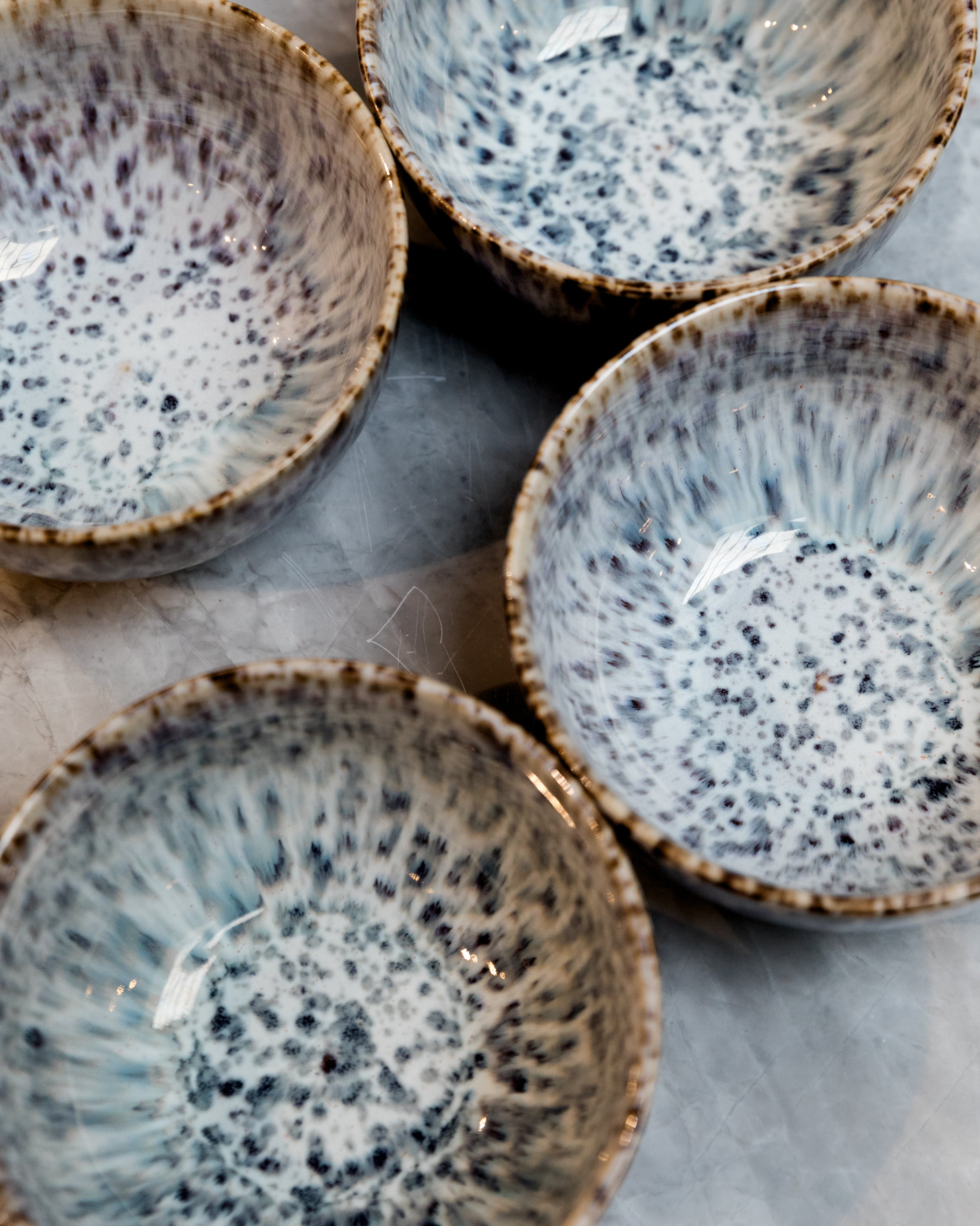 Set of four ceramic bowls with speckled glaze on a marble surface