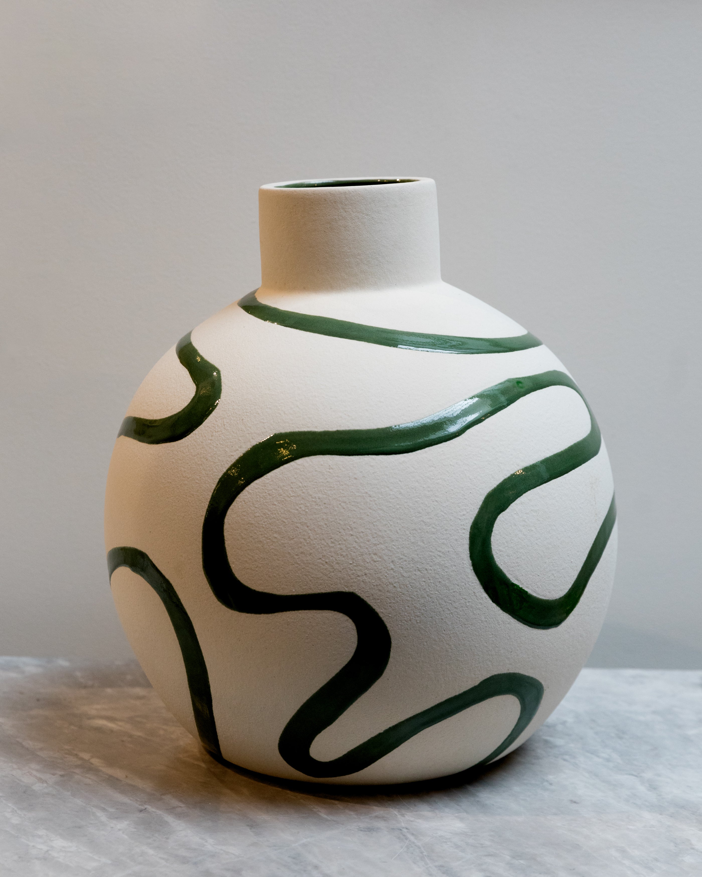 White vase with green wavy patterns on a light gray background