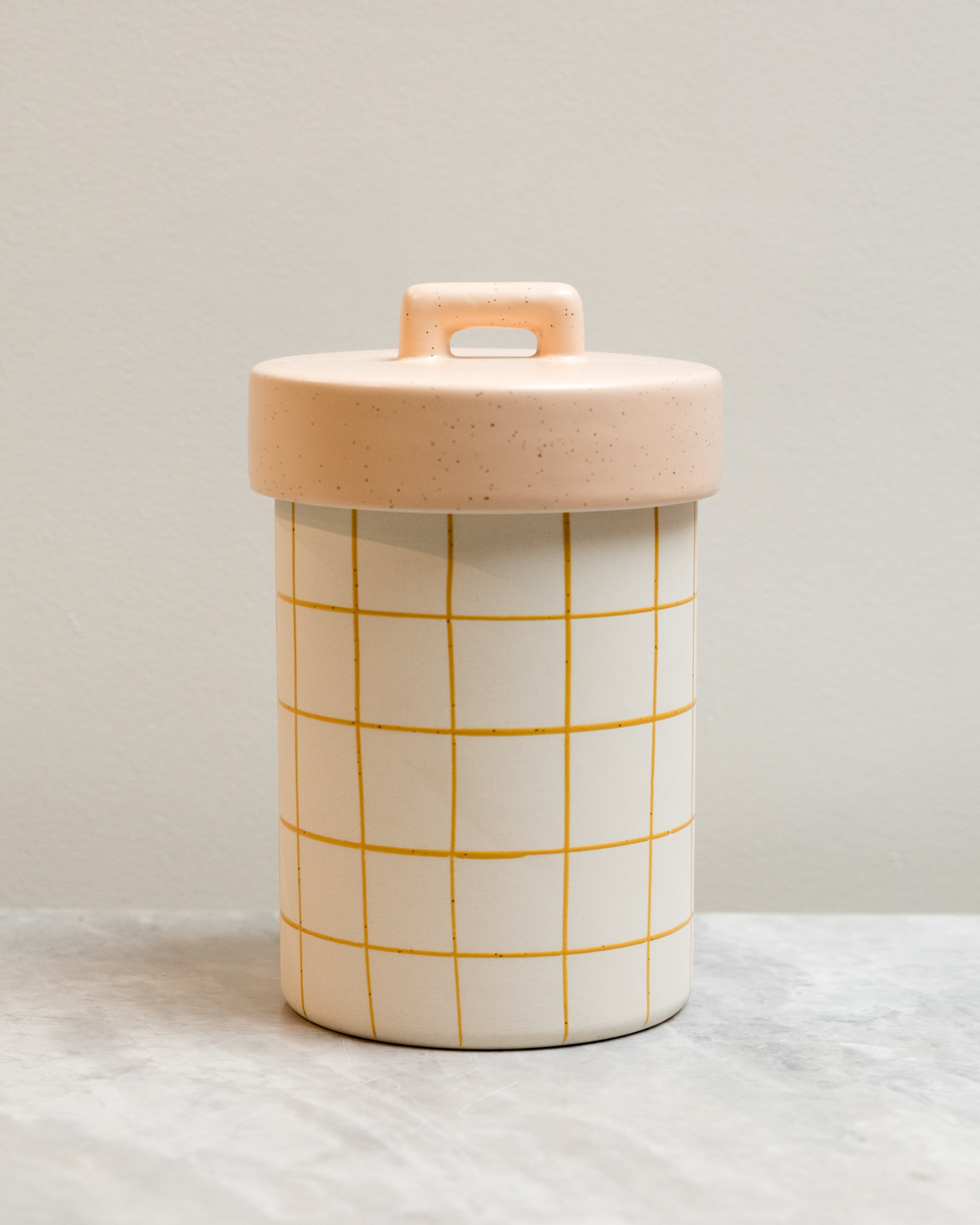 Cylindrical container with grid pattern and pink lid on a neutral background