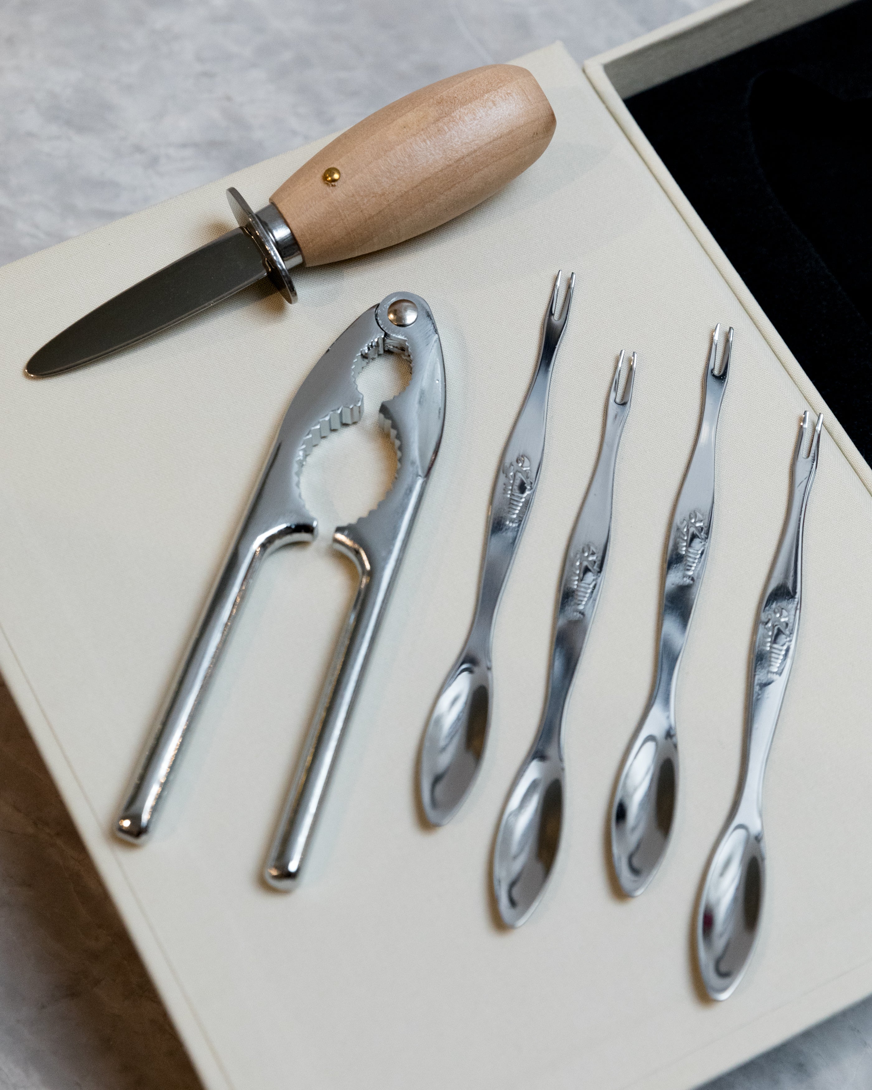 Set of silver utensils including a knife, cracker, and seafood utensils on a light surface.