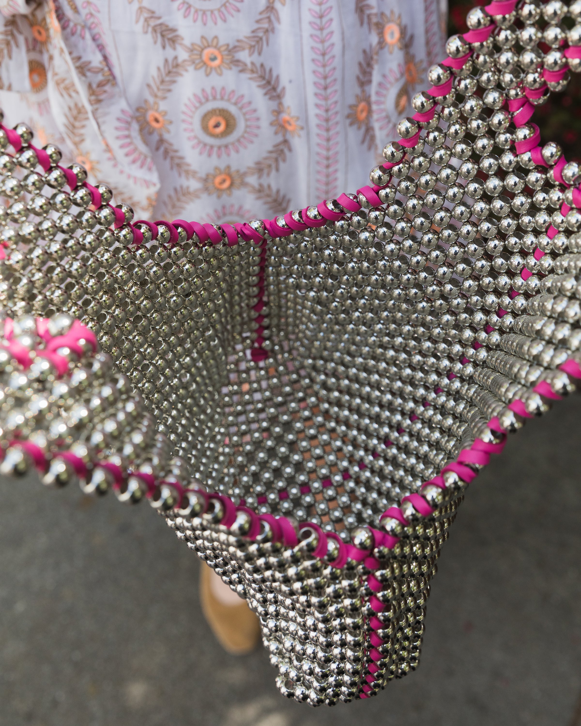 Close-up of a garment with silver beading and pink accents on a blurred background