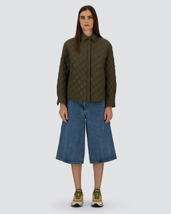 Person wearing a green quilted jacket and blue jeans on a white background