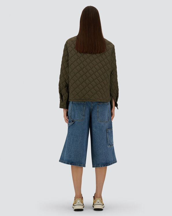 Person wearing a green quilted jacket and blue jeans on a white background