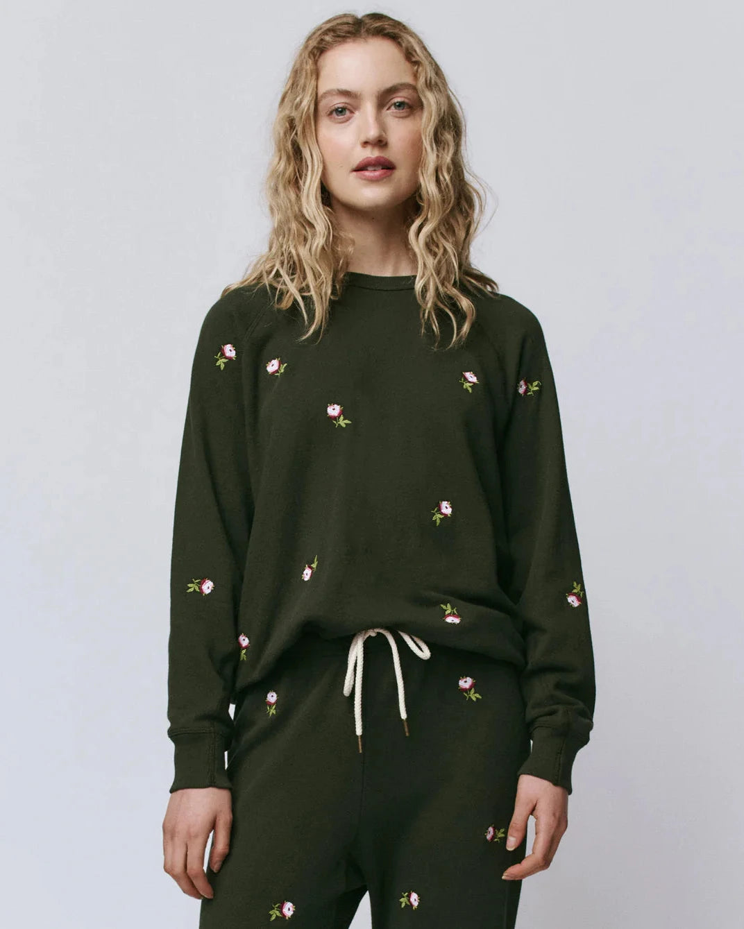 Woman wearing a dark green sweatshirt with floral embroidery on a plain background