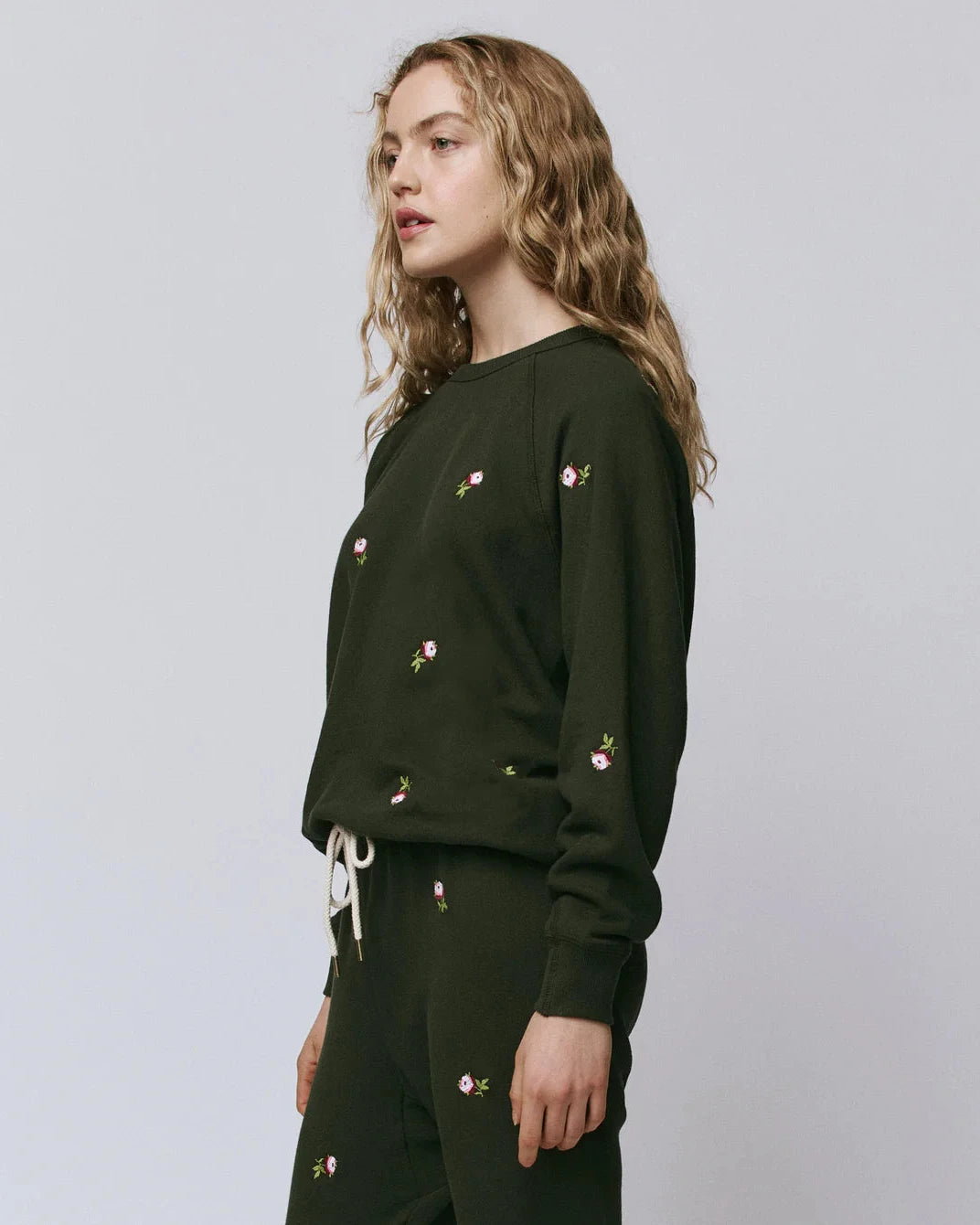 Woman wearing a dark green sweatshirt with floral embroidery on a plain background