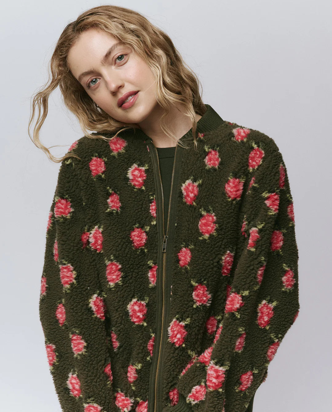 Woman wearing a dark green jacket with pink floral patterns on a light gray background