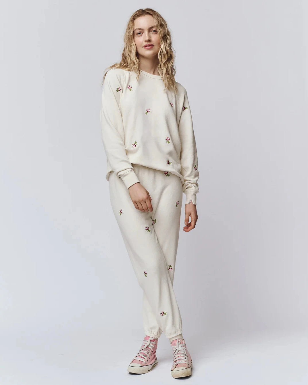 Woman wearing a cream-colored outfit with floral embroidery on a white background