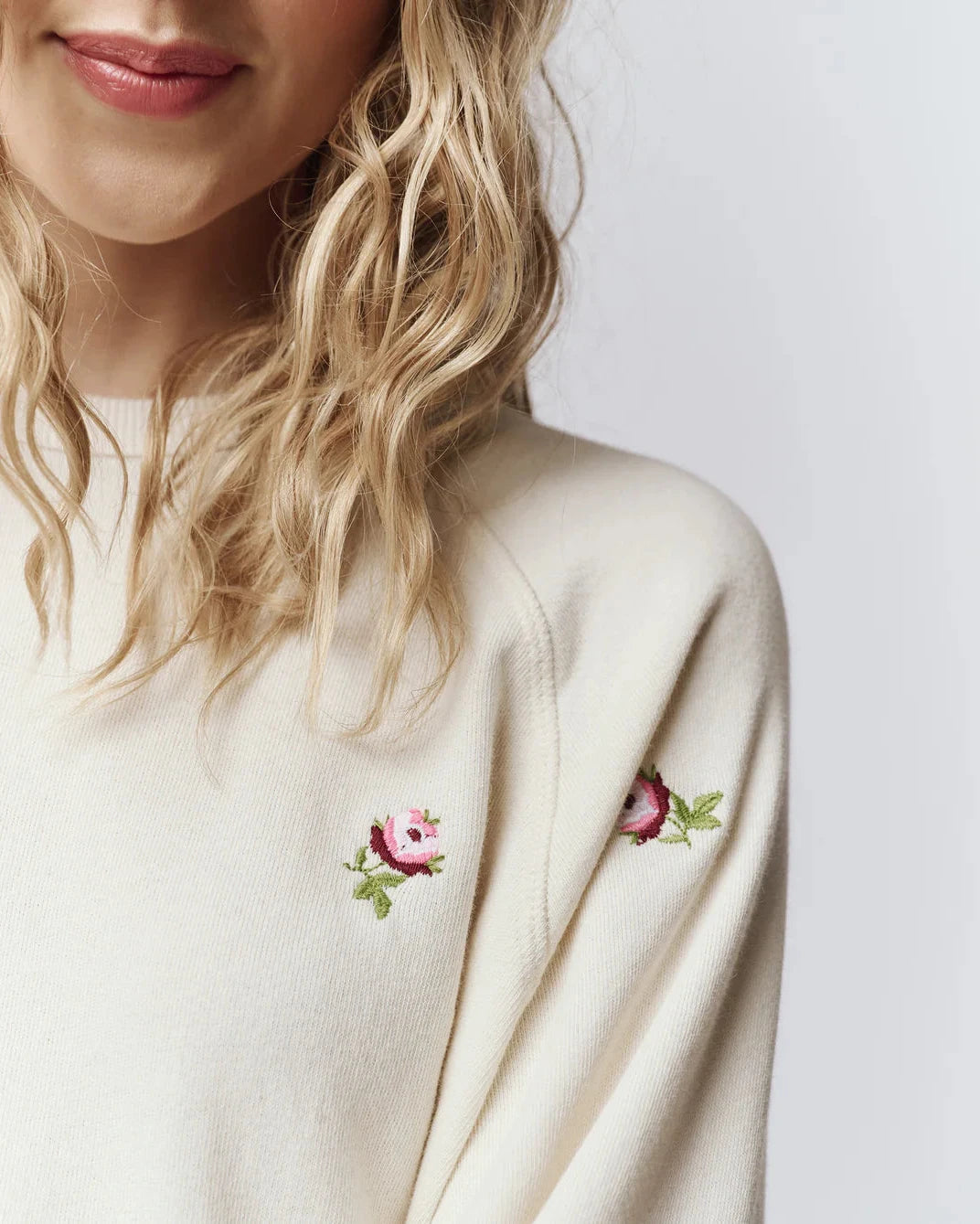 White sweater with floral embroidery on a plain background
