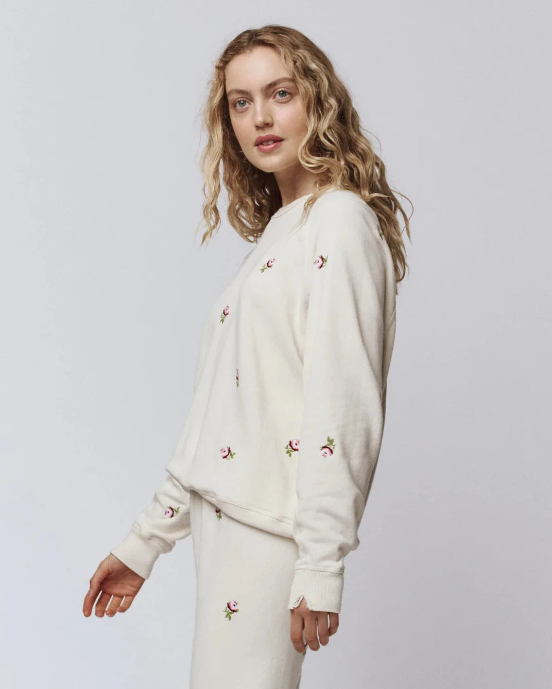 Woman wearing a cream-colored outfit with floral embroidery on a plain background