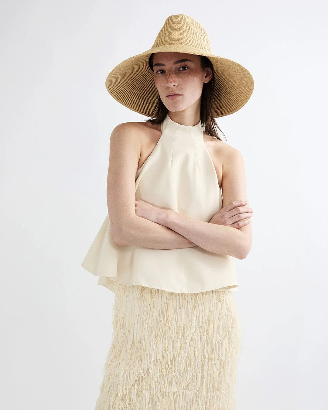 Woman wearing a beige halter top and skirt with a wide-brimmed hat on a white background
