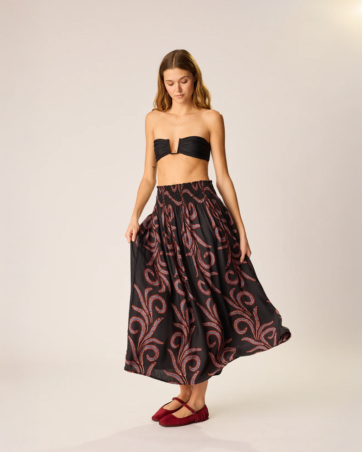 Woman wearing a black strapless top and patterned skirt on a plain background
