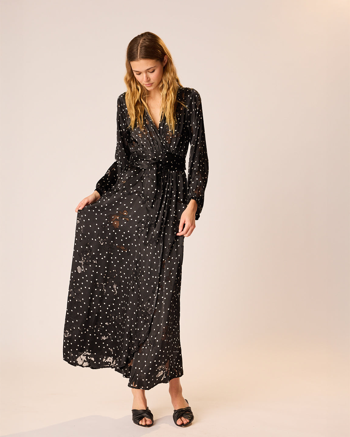 Woman wearing a black long-sleeve dress with white polka dots on a beige background