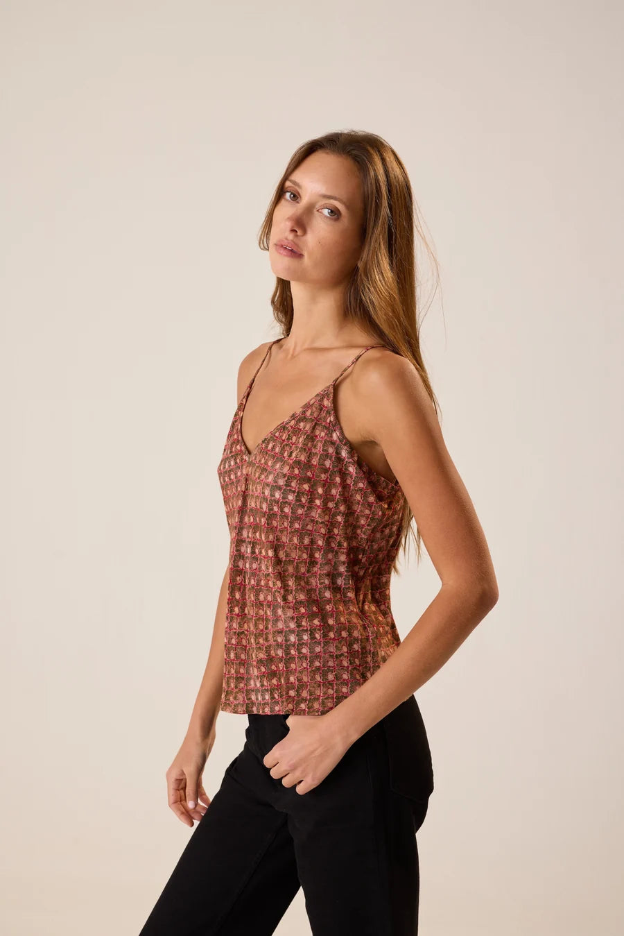 Woman wearing a patterned top and black pants against a plain background