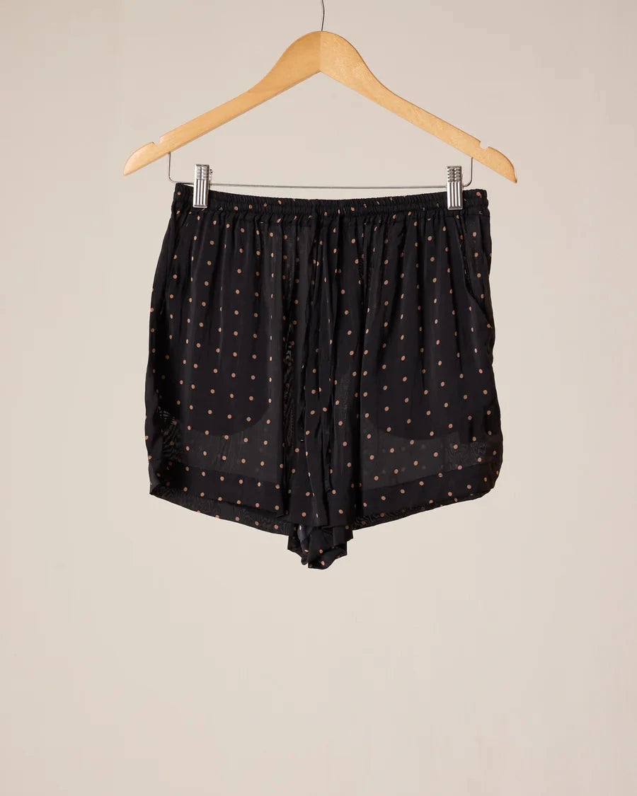 Black sheer shorts with a small white polka dot pattern, hanging from a wooden hanger against a plain beige background.