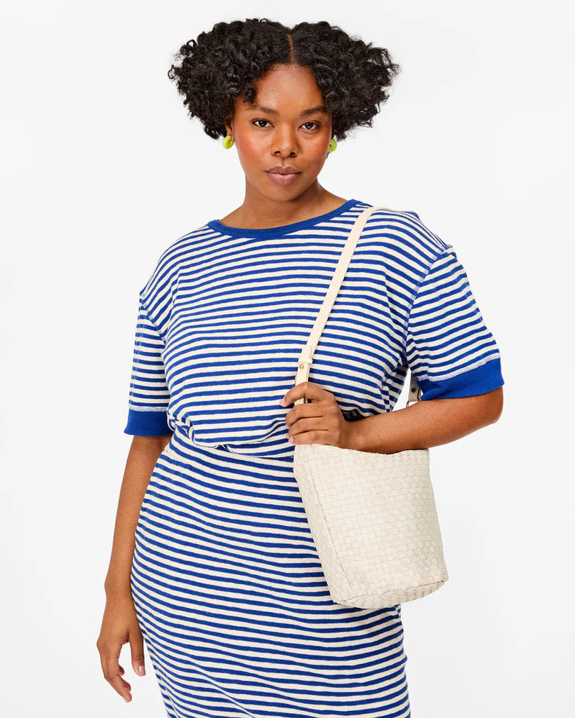Woman wearing a blue and white striped dress holding a white tote bag on a plain background