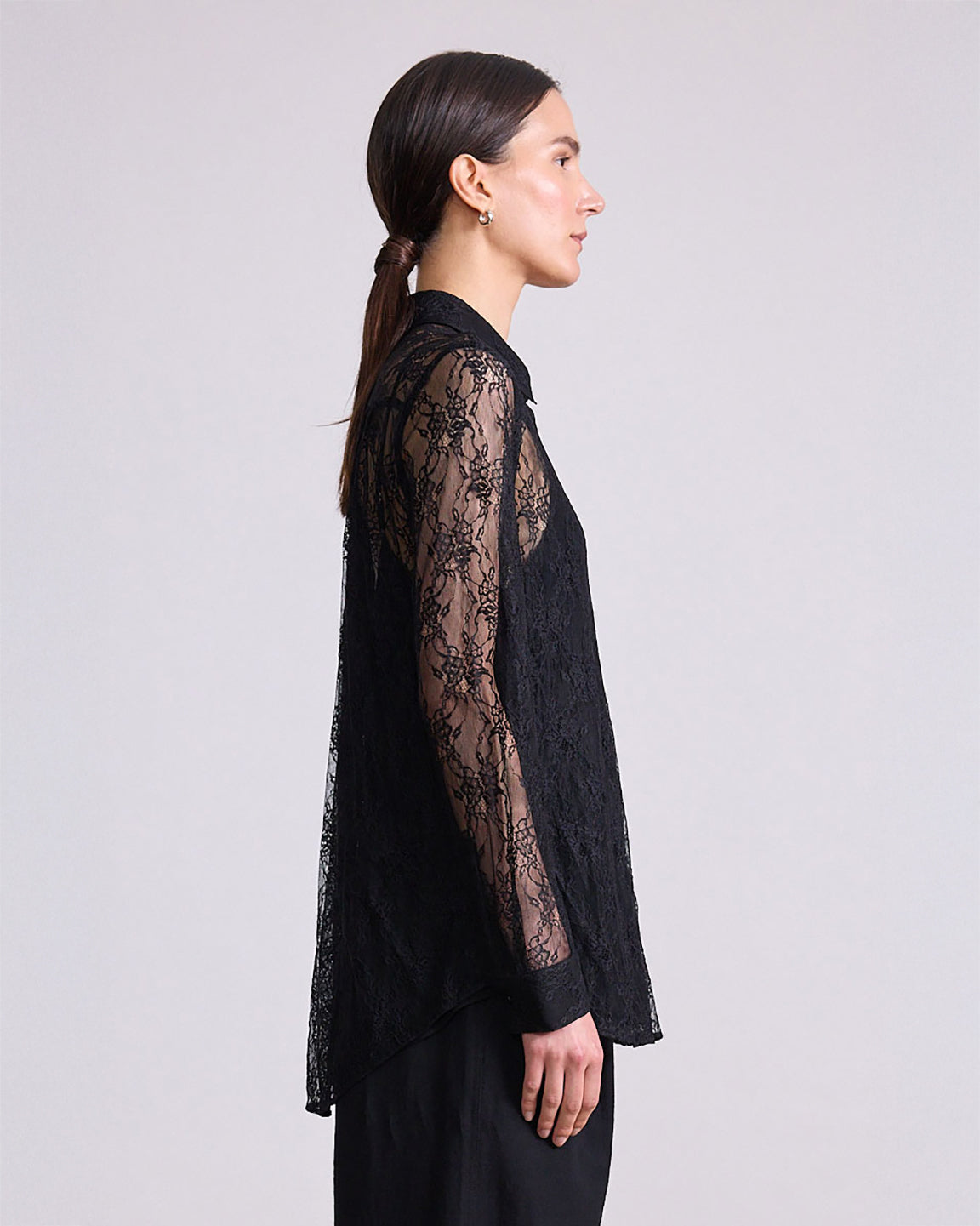 Woman wearing a black lace top against a plain background