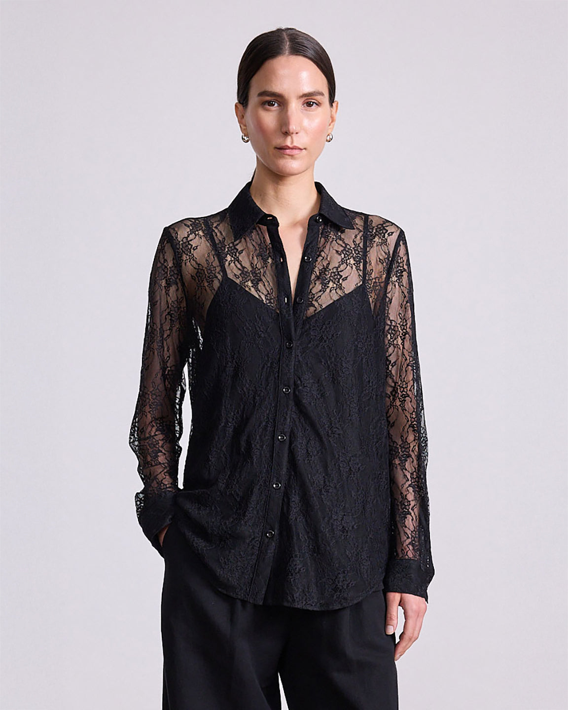 Woman wearing a black lace-trimmed shirt against a plain background