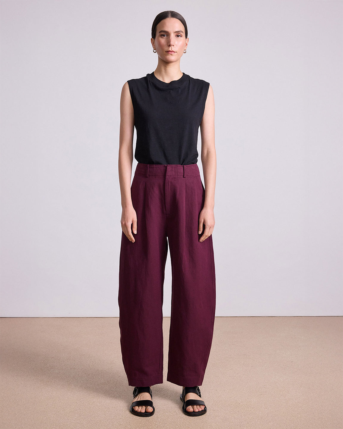 Woman wearing a black sleeveless top and burgundy pants on a plain background