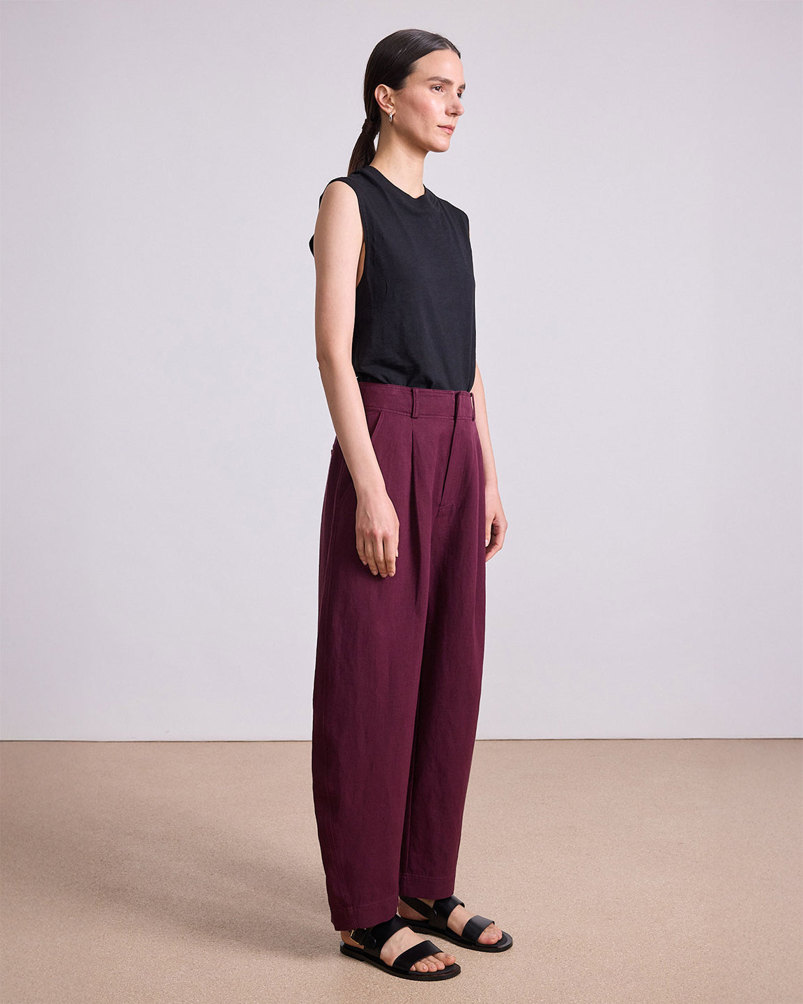 Woman wearing a black sleeveless top and maroon pants against a plain background