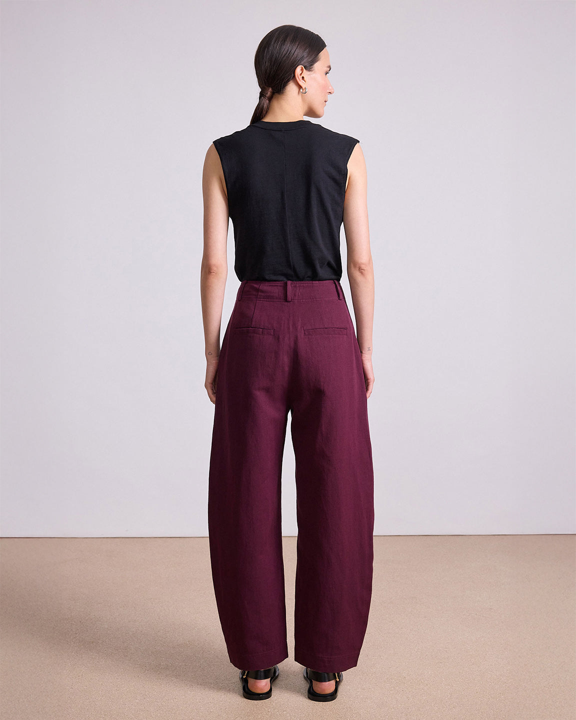 Woman wearing a black sleeveless top and maroon wide-leg pants on a plain background