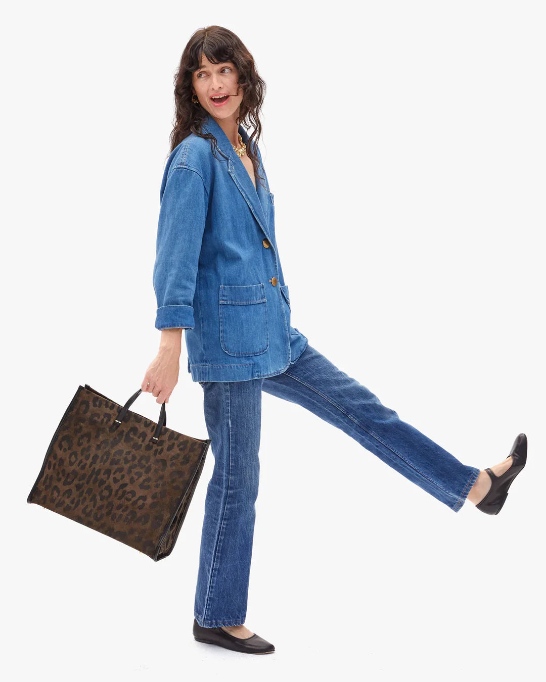 Woman in a denim outfit holding a leopard print bag on a white background