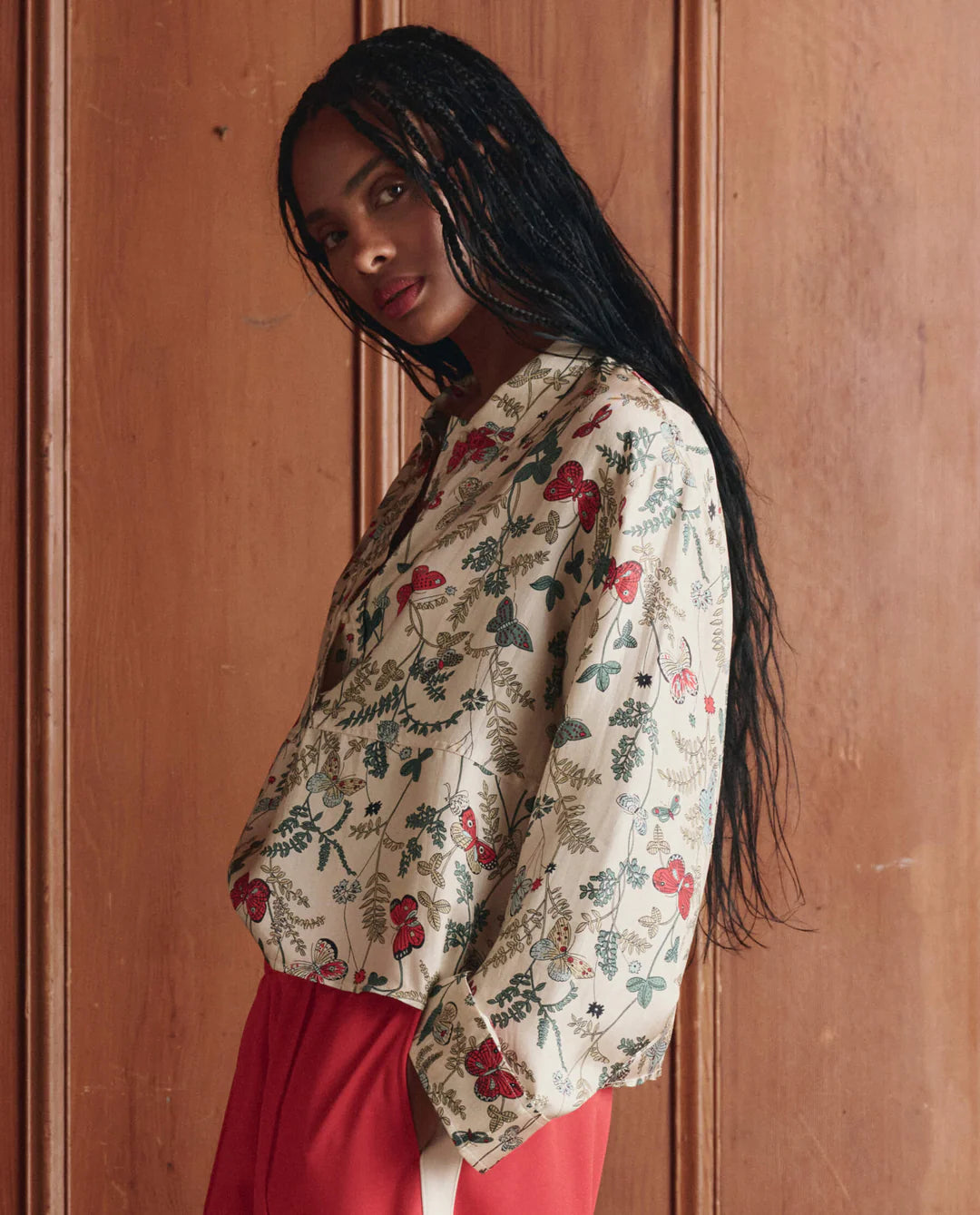 Woman wearing a floral blouse and red pants against a wooden panel background