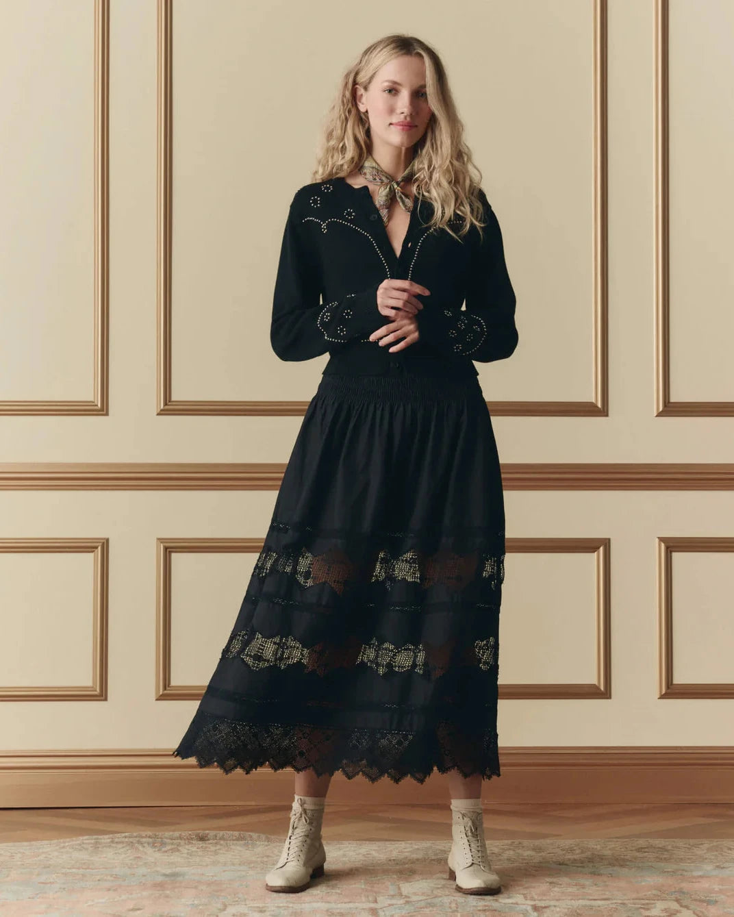 Woman wearing a black dress with lace details against a beige wall.