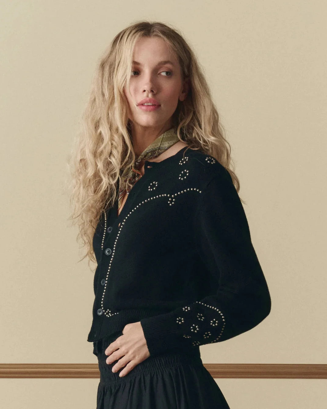 Woman wearing a black embroidered top against a beige wall